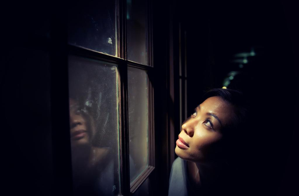 Woman looking through a window. Her reflection shows in the windowpane.