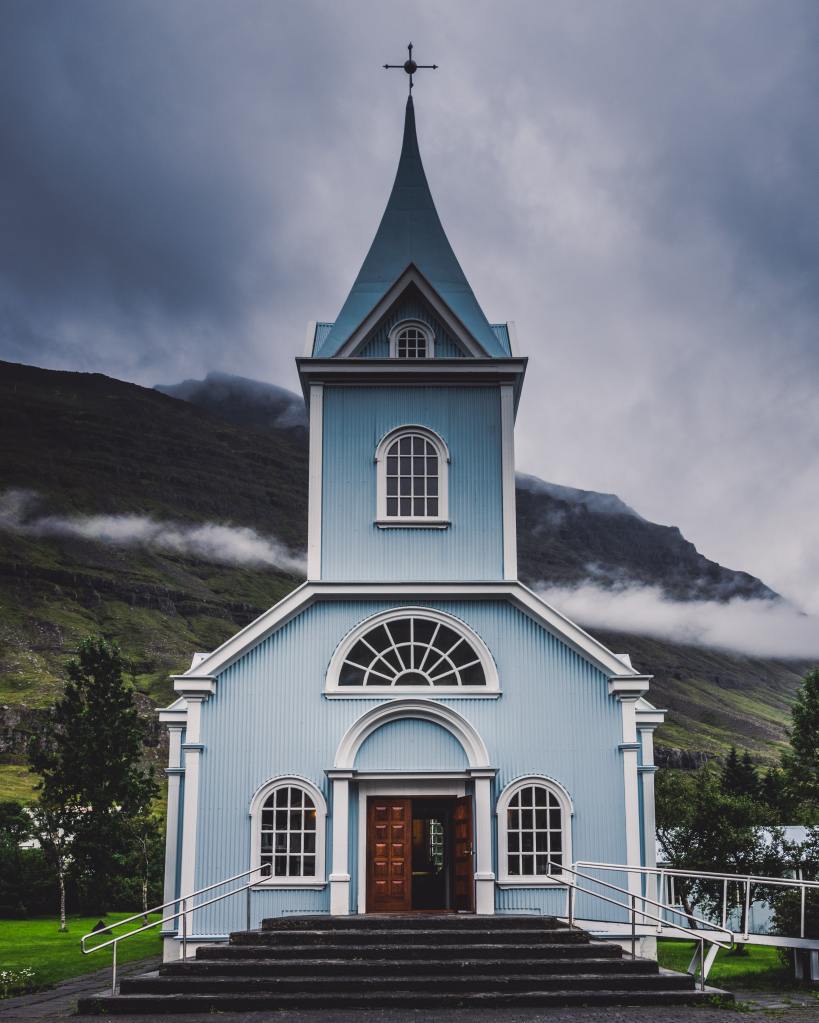 Front of a small wooden church painted light blue in the mountains