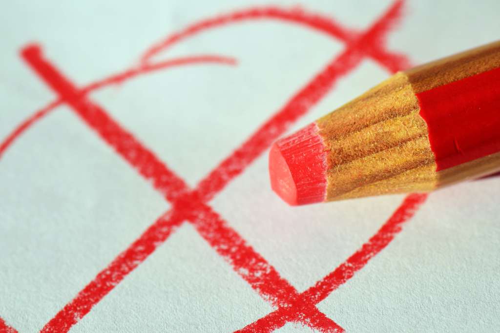 Close up of a red pencil and a red x drawn on white paper