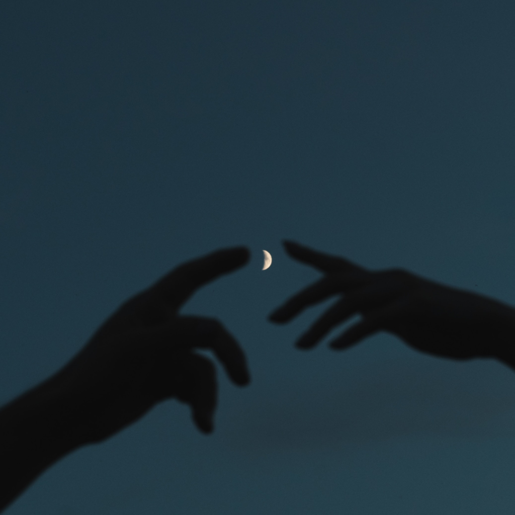 Silhouettes of two hands pointing toward a waxing crescent moon